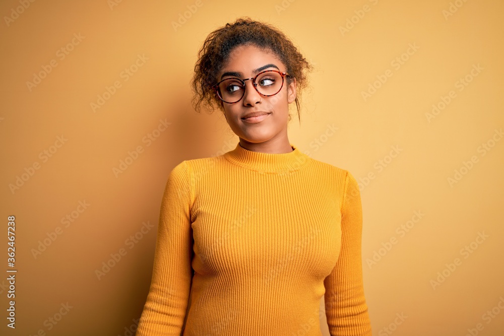 Young beautiful african american girl wearing sweater and glasses over yellow background smiling looking to the side and staring away thinking. Young beautiful african american girl wearing sweater and glasses over yellow background smiling looking to the side and staring away thinking.