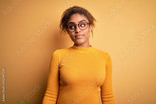 Young beautiful african american girl wearing sweater and glasses over yellow background smiling looking to the side and staring away thinking.