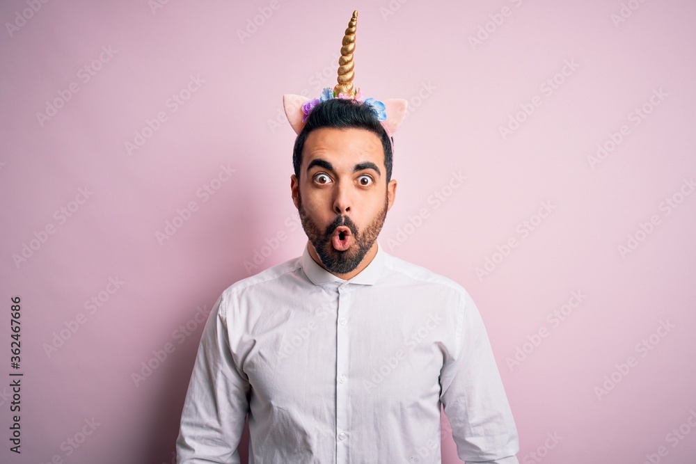 Φωτογραφία Young handsome man with beard wearing funny unicorn diadem over pink background afraid and shocked with surprise expression, fear and excited face