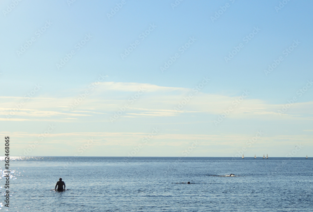 Summer sea background with silhouettes of people in the water.