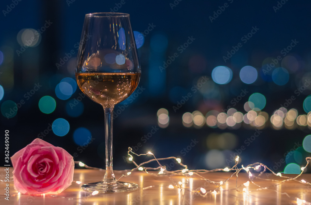 A glass of Rose wine with rose flower on table and colorful city bokeh light background. - obrazy, fototapety, plakaty 