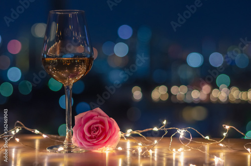 A glass of Rose wine with rose flower on table and colorful city bokeh light background.