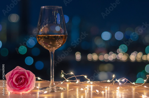 A glass of Rose wine with rose flower on table and colorful city bokeh light background.
