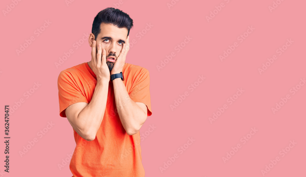 Fototapeta premium Young handsome man with beard wearing casual t-shirt tired hands covering face, depression and sadness, upset and irritated for problem