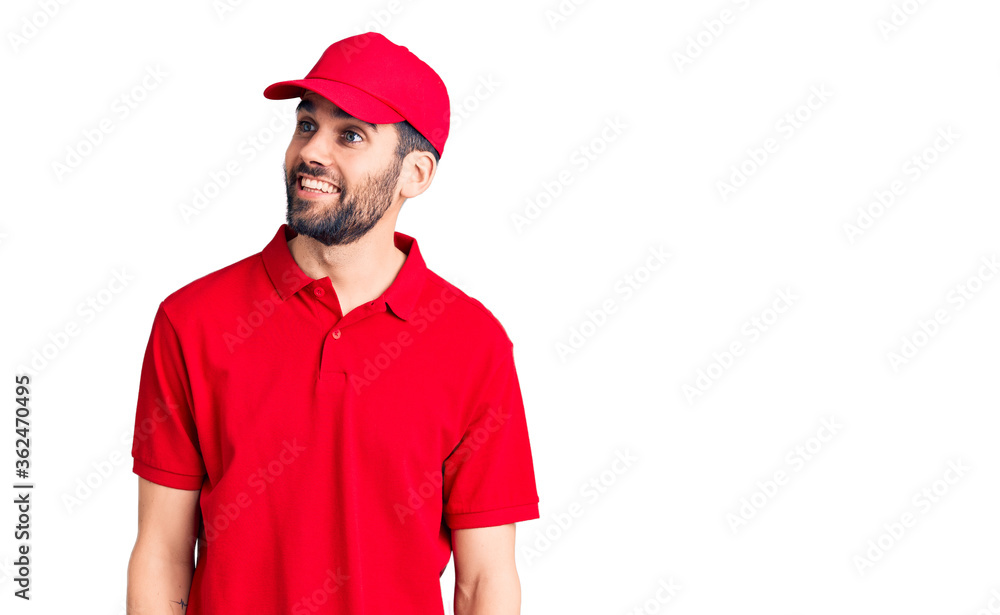 Young handsome man with beard wearing delivery uniform looking away to side with smile on face, natural expression. laughing confident.