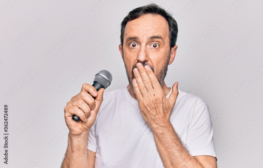 Middle age handsome singer man singing using microphone over isolated white background covering mouth with hand, shocked and afraid for mistake. Surprised expression Middle age handsome singer man singing using microphone over isolated white background covering mouth with hand, shocked and afraid for mistake. Surprised expression
