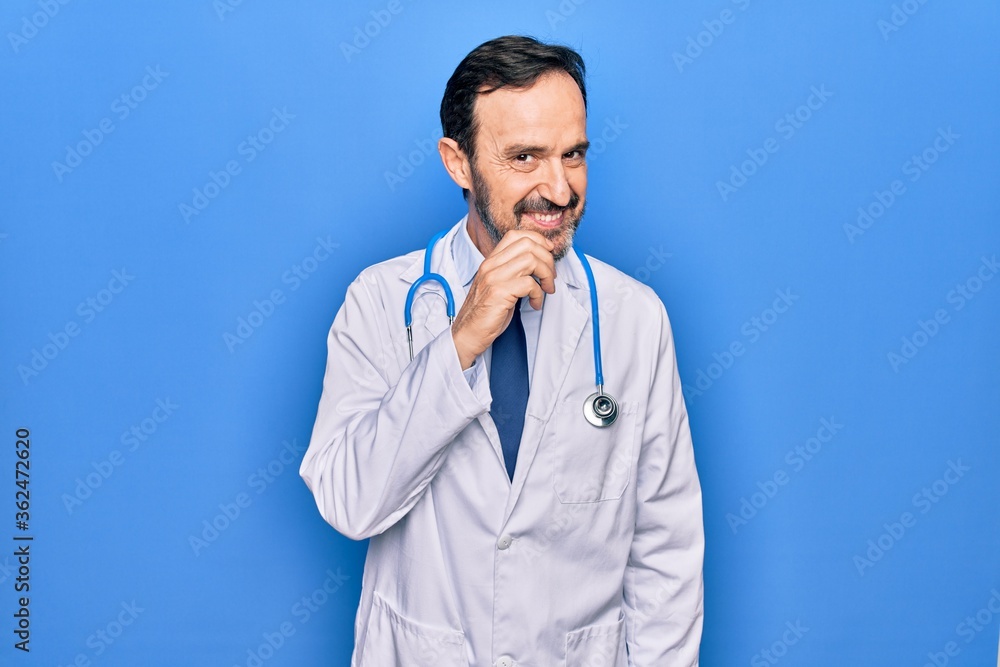 Middle age handsome doctor man wearing coat and stethoscope over isolated blue background smiling looking confident at the camera with crossed arms and hand on chin. Thinking positive. Middle age handsome doctor man wearing coat and stethoscope over isolated blue background smiling looking confident at the camera with crossed arms and hand on chin. Thinking positive.