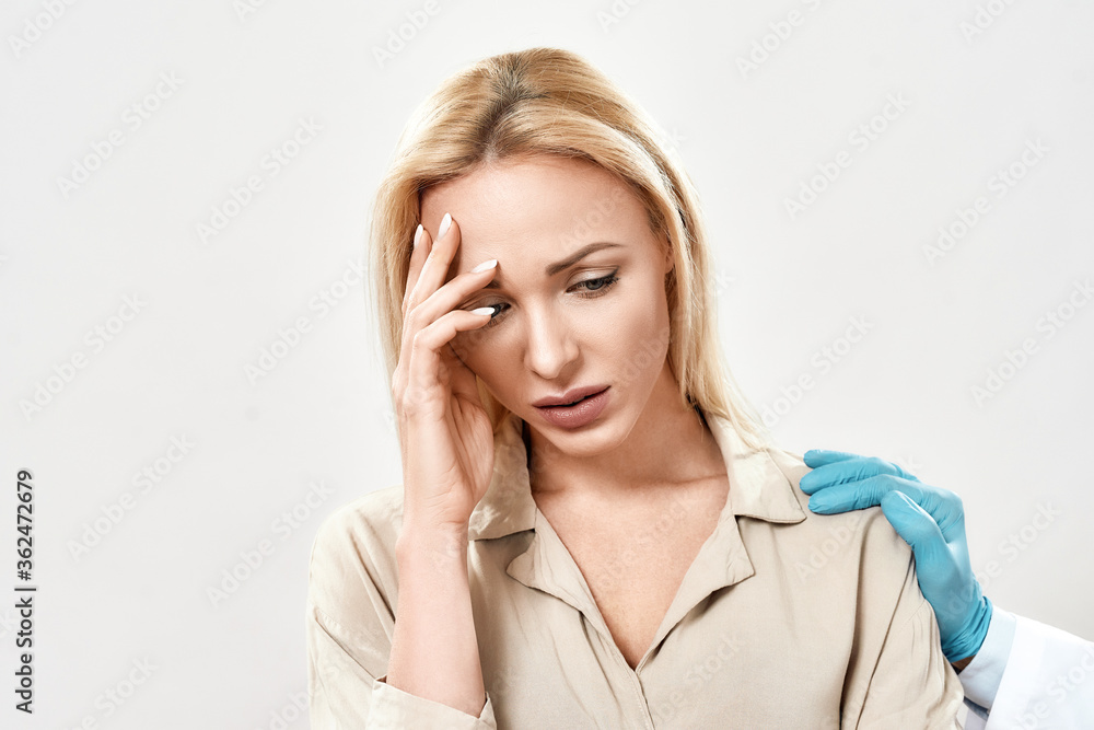 Portrait of depressed young woman visiting doctor. Doctor in blue sterile gloves supporting and comforting upset female patient standing against grey background in studio Portrait of depressed young woman visiting doctor. Doctor in blue sterile gloves supporting and comforting upset female patient standing against grey background in studio