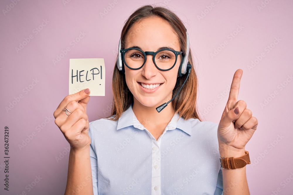 Beautiful call center agent woman working using headset holding help reminder message surprised with an idea or question pointing finger with happy face, number one Beautiful call center agent woman working using headset holding help reminder message surprised with an idea or question pointing finger with happy face, number one