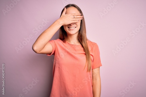 Young beautiful woman wearing casual t-shirt standing over isolated pink background smiling and laughing with hand on face covering eyes for surprise. Blind concept.