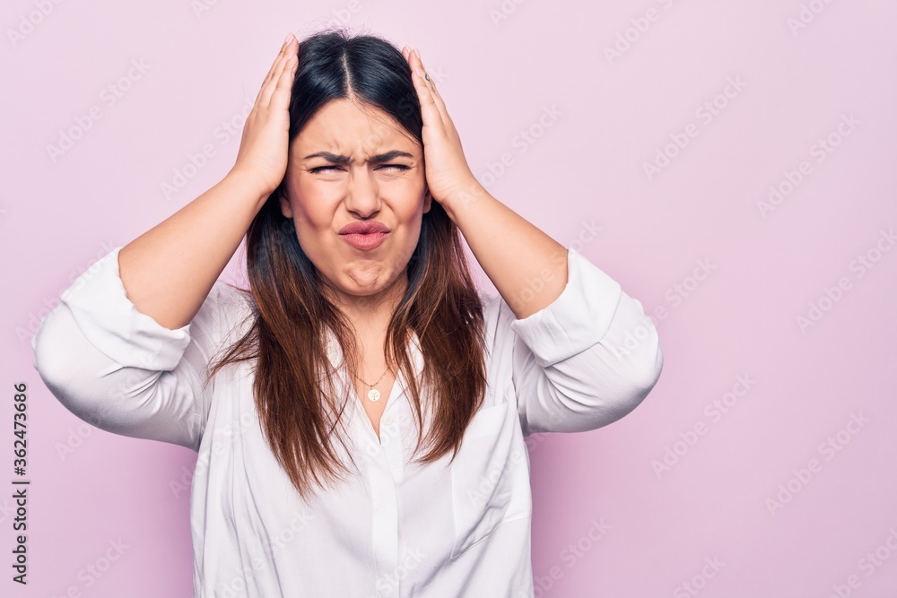 Young beautiful brunette woman wearing elegant shirt standing over isolated pink background with hand on head, headache because stress. Suffering migraine.