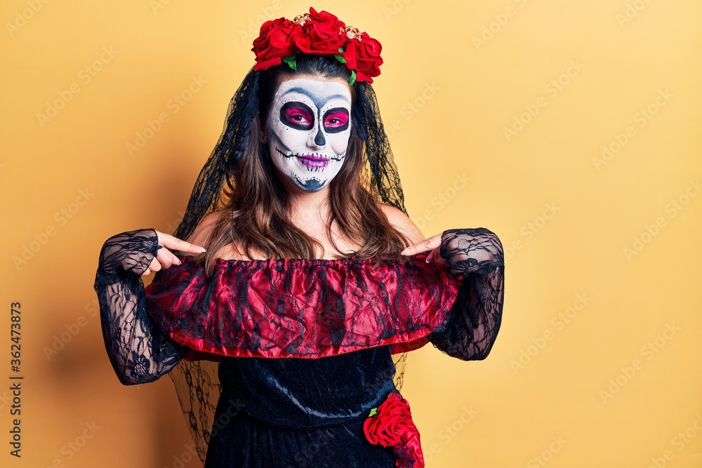 Young woman wearing day of the dead costume over yellow looking confident with smile on face, pointing oneself with fingers proud and happy.