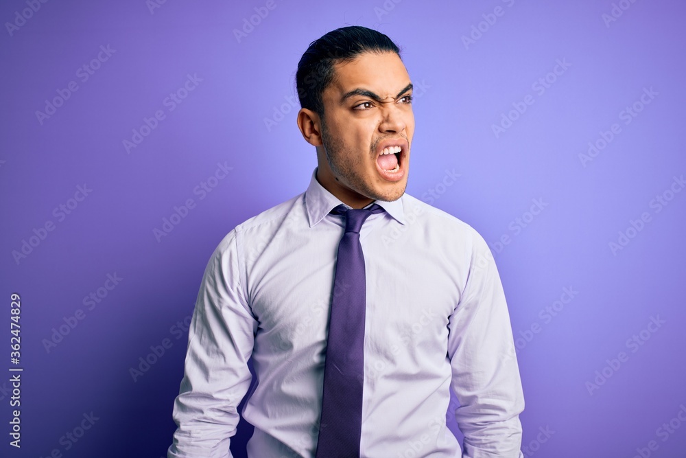 Young brazilian businessman wearing elegant tie standing over isolated purple background angry and mad screaming frustrated and furious, shouting with anger. Rage and aggressive concept. Young brazilian businessman wearing elegant tie standing over isolated purple background angry and mad screaming frustrated and furious, shouting with anger. Rage and aggressive concept.