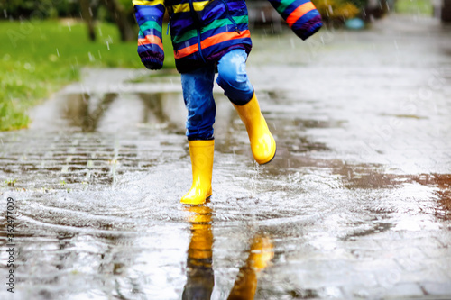 Close-up of kid wearing yellow rain boots and walking during sleet, rain and snow on cold day. Child in colorful fashion casual clothes jumping in a puddle. Having fun outdoors