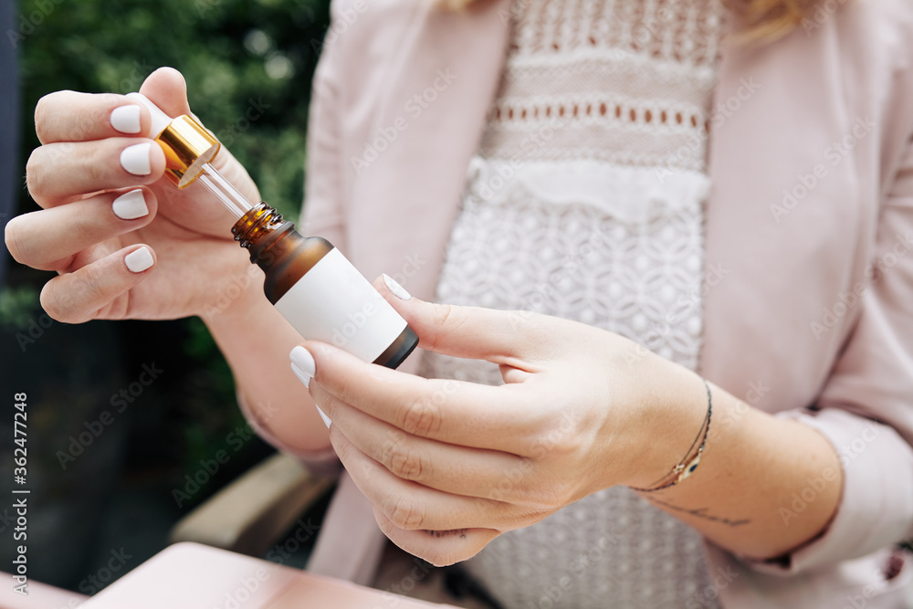 Obraz premium Close-up image of young businesswoman opening small bottle of essential oil or serum