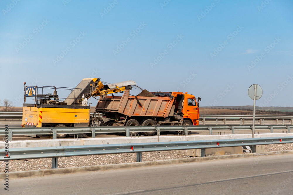Dismantling of asphalt pavement. Road works. Recycled asphalt crumb is poured over the conveyor belt into the truck body Dismantling of asphalt pavement. Road works. Recycled asphalt crumb is poured over the conveyor belt into the truck body