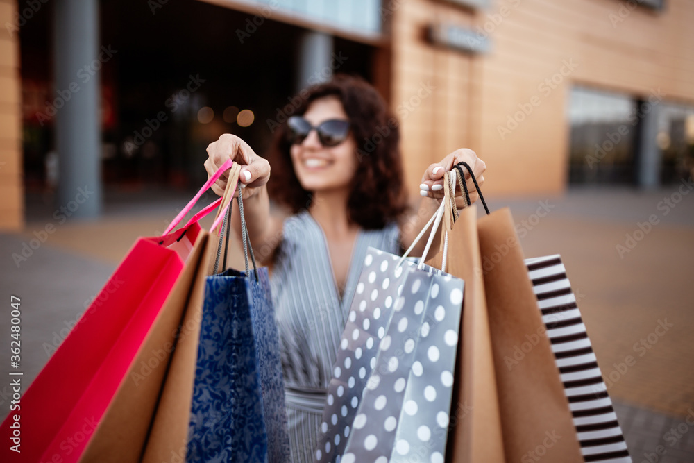 Young beautiful woman shopaholic walks out the shopping center with a pack of bags with purchases. Pink shopper in the hand of an obssessed girl. Shopping, clothes and spending money concept. Young beautiful woman shopaholic walks out the shopping center with a pack of bags with purchases. Pink shopper in the hand of an obssessed girl. Shopping, clothes and spending money concept.