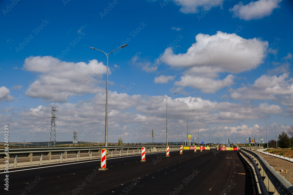 New asphalt road with road lamps on a background of blue sky with white clouds.