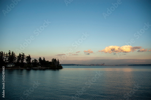 View of Seattle skyline across Puget Sound from Bainbridge Island ferry at dusk. Blue sky and clouds.