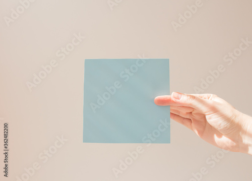  Blue square leaflet with hard shadows mock up on a white background in the hand of a young woman. School concept