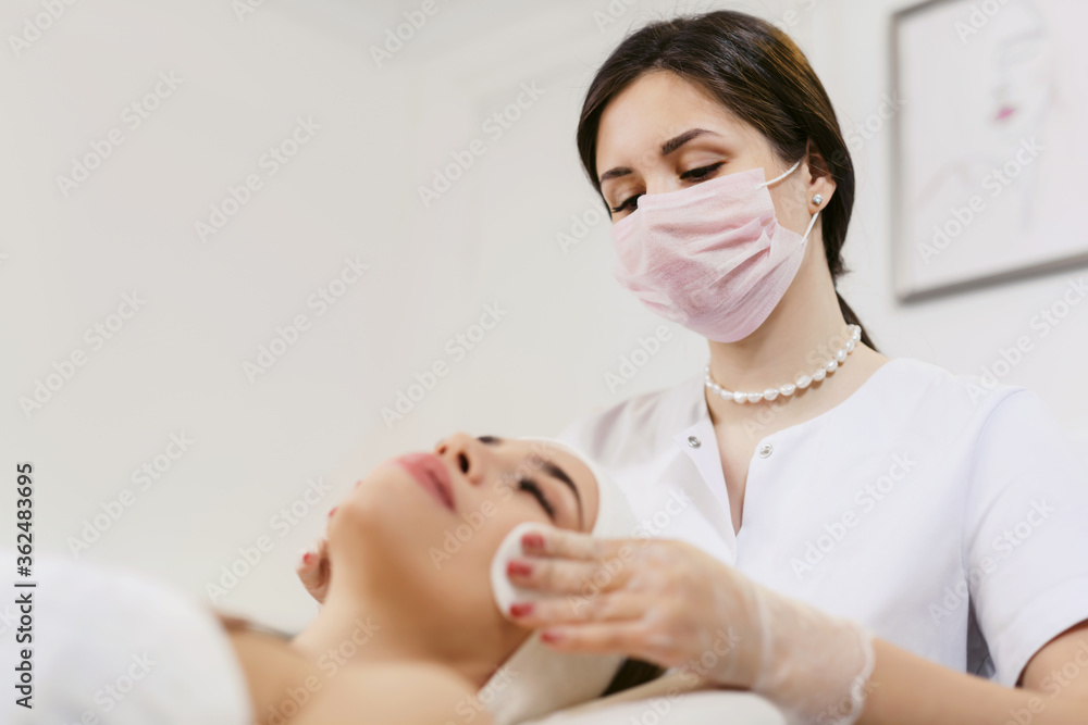 Close up of beautician hands doing facial cleansing of a young woman using cotton pads or sponge in a beauty clinic or spa. Cosmetology treatment. Perfect skin concept. Eternal youth.