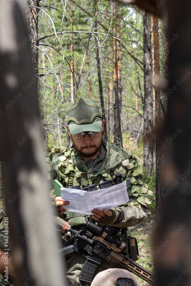 Naklejka premium Fully armed american soldier is reviewing a document on military range, active military game airsoft, vertikal image