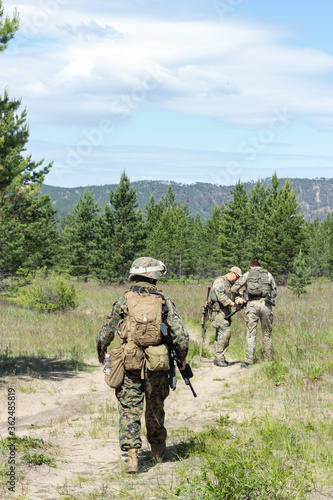 Group of fully armed american soldiers on the summer forest road on military range, active military game airsoft.