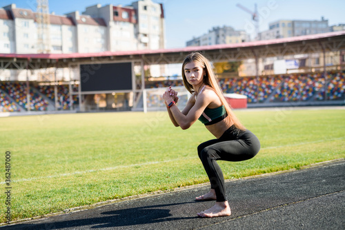 Morning exercises on stadium. Young, sporty and slim woman making exercises