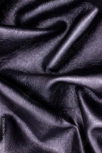 Black artificial skin close-up. Textile material, sloppy folds. Black leather background
