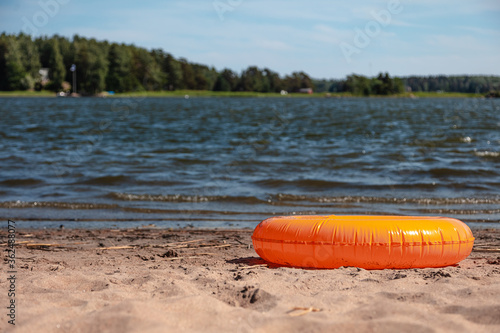 Orange rubber ring for swimming on the sandy shore at the edge of the