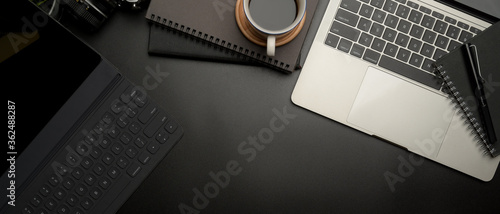 Dark modern workspace with digital tablet, laptop, coffee cup, schedule books and copy space