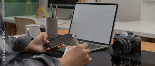 Female worker taking note on digital tablet while looking information on smartphone and mock-up laptop