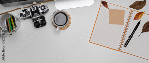 Minimal workspace with blank notebook, copy space, coffee cup, and camera on white desk