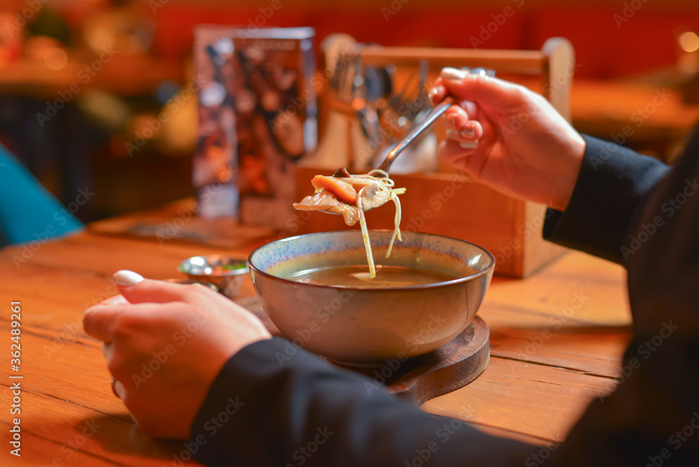 Young woman eating soup served in a white bowl. Eating out. Restaurant concept. Woman' s hand holding spoon.