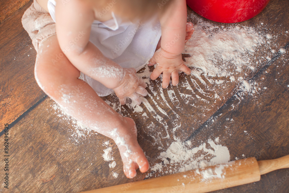 A one year old girl is playing with flour. Rolling pin. Cooking pancakes.