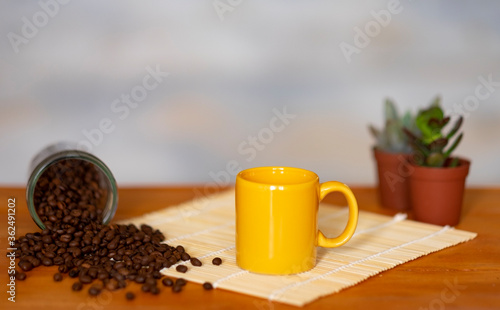 Espresso coffee in yellow ceramic cup, coffee beans on wooden table - small succulent plants on background