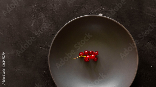 Red currant bunch in empty bowl on textured chalkboard background with copy space. Dark Moody picture. Minimalism about organic berries, contrast, fresh food and ingredien for desserts