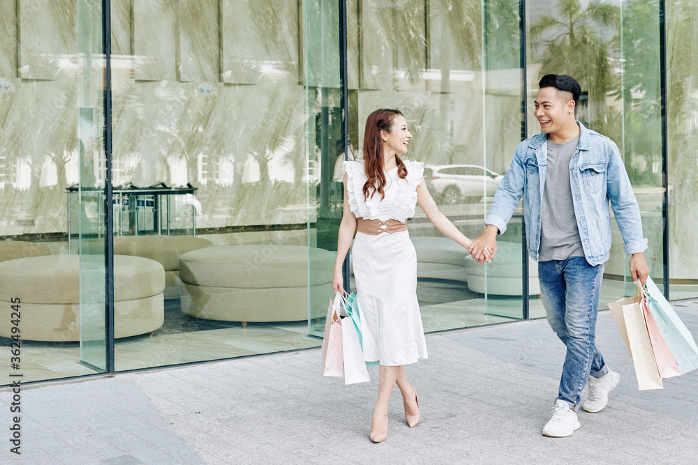 Happy beautiful young Vietnamese woman pulling hand of boyfriend when walking to another shop Happy beautiful young Vietnamese woman pulling hand of boyfriend when walking to another shop