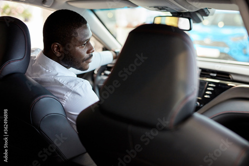 successful confident businessman sits behind the wheel of new automobile, handsome african guy enjoy design and convenience of auto