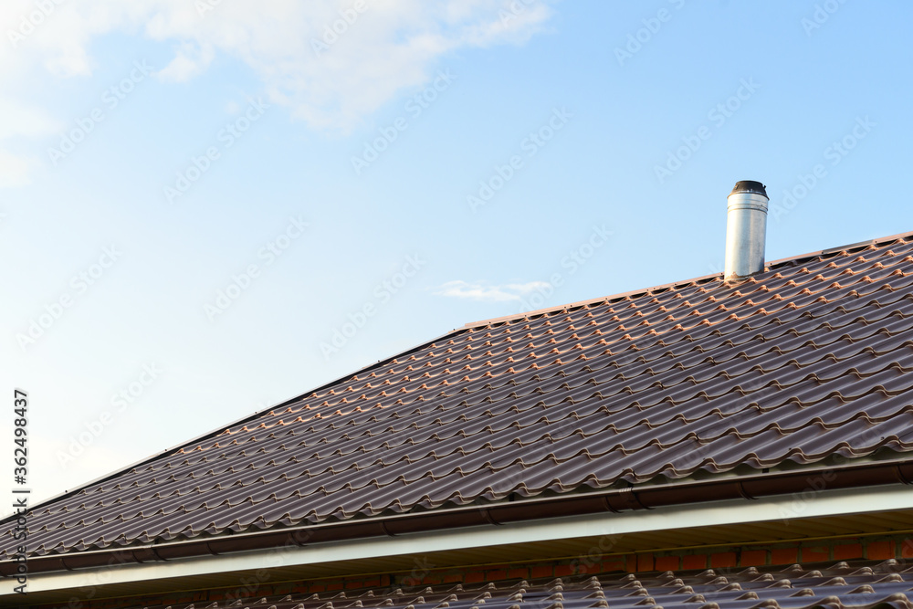 The roof of the house is made of sheets of brown metal tiles with a pipe