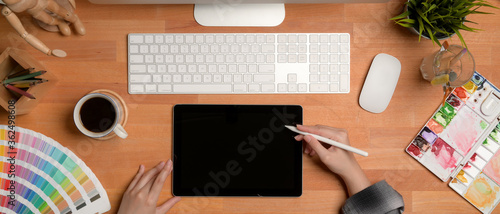 Female artist working on wooden table with digital tablet, computer, painting tools and decorations