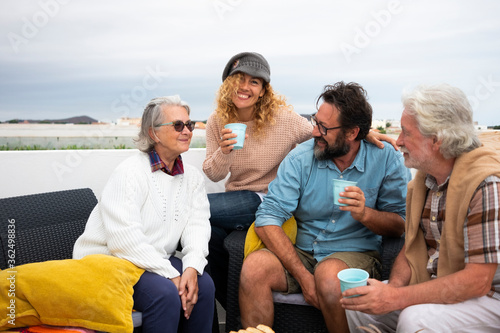 Cheerful group of women and men, multi-generation family having fun together outdoor on terrace. Four people from senior to middle age, parents with grandparents
