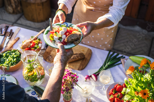 Catering service outdoors. Enjoy fresh caprese salad with mozzarella and baguette. Woman serving vegetarian food on plate to another person at garden party