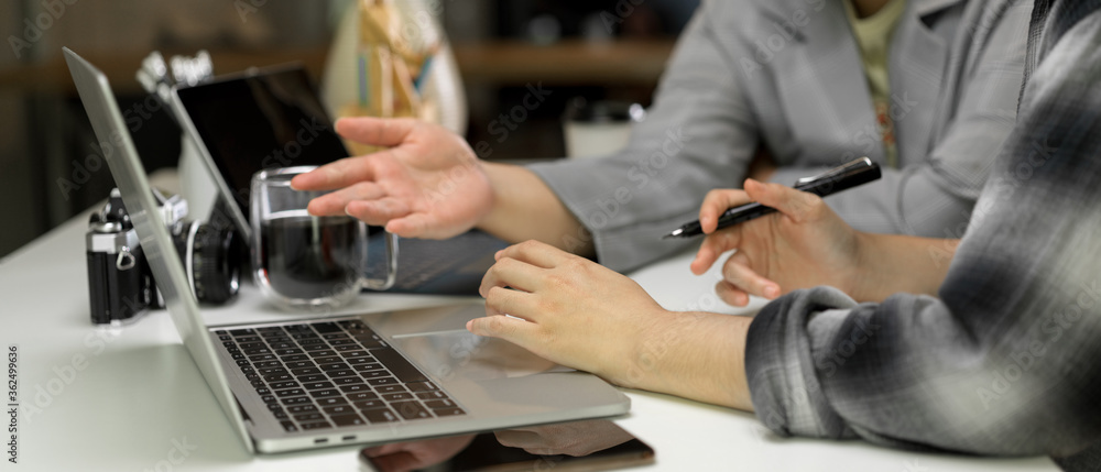 Two female workers discussing on their project with laptop on white table with camera and supplies
