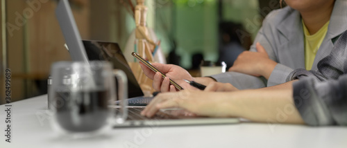 Female workers consulting on their work with smartphone and laptop in minimal office room