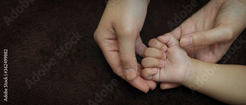 Tiny hand newborn baby in mother hands on dark background