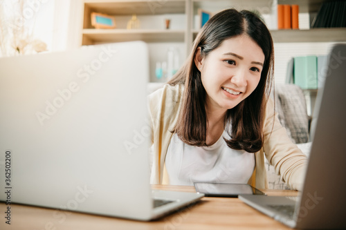 Beautiful asian woman get new normal life, social distancing. Young business woman work at home by using laptop computer, conference with happiness and smiley face Pretty girl get relax