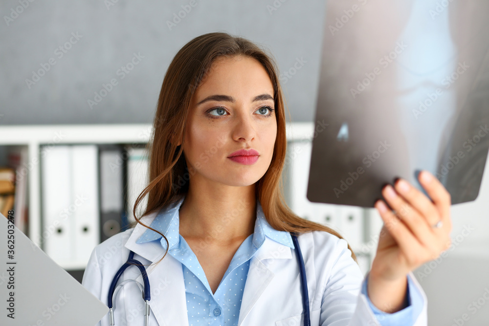 Beautiful female doctor hold in arm and look at xray photography portrait. Skeleton bone disease exam medic aid or cancer physical test in hospital for healthy lifestyle education career concept Beautiful female doctor hold in arm and look at xray photography portrait. Skeleton bone disease exam medic aid or cancer physical test in hospital for healthy lifestyle education career concept