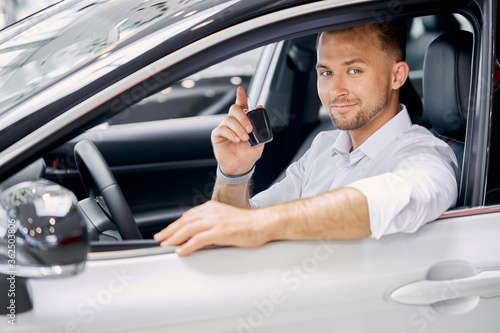 new happy car owner in dealership. man got keys of car, the perfect luxurious white auto now is his property. man sits behind the wheel and look at camera