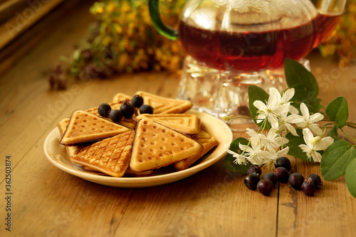 The composition of tea with homemade biscuits and berries, and flowers of clematis on wooden background